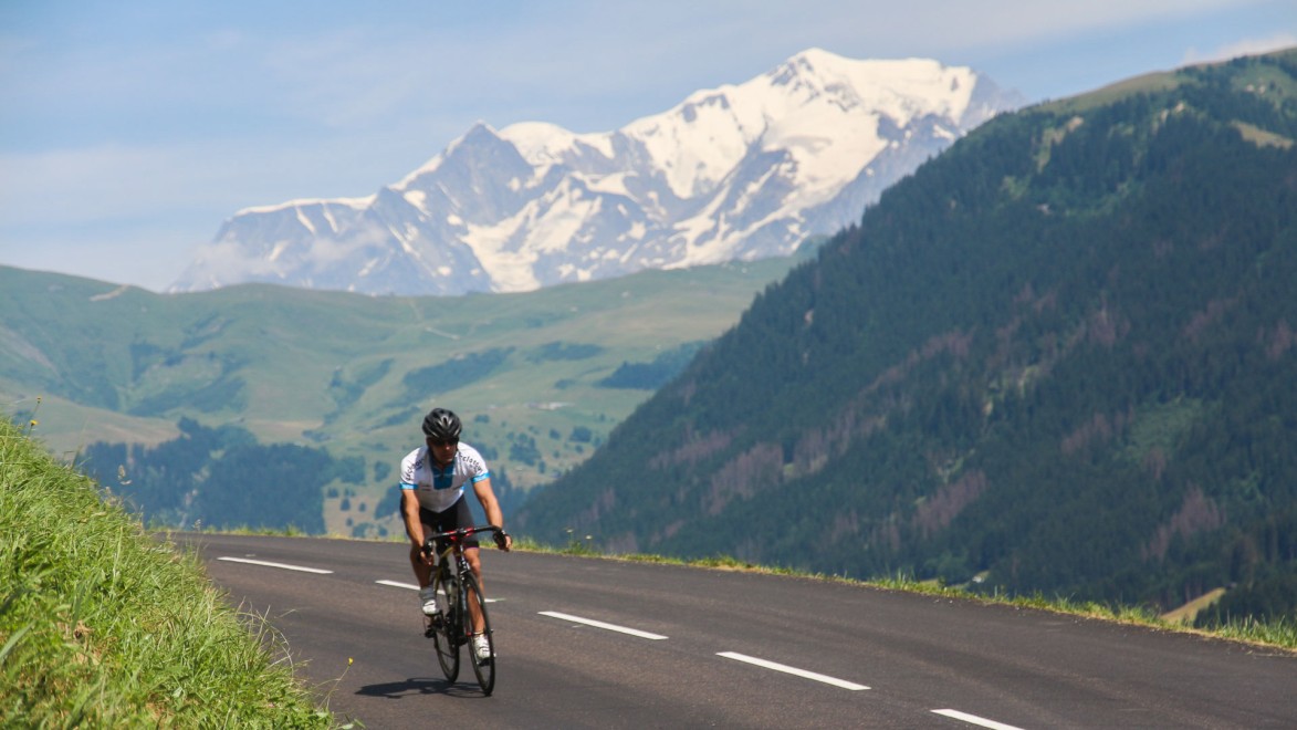 A cyclist on the Col des Saisies mountain road with the summit of Mont Blanc in the background