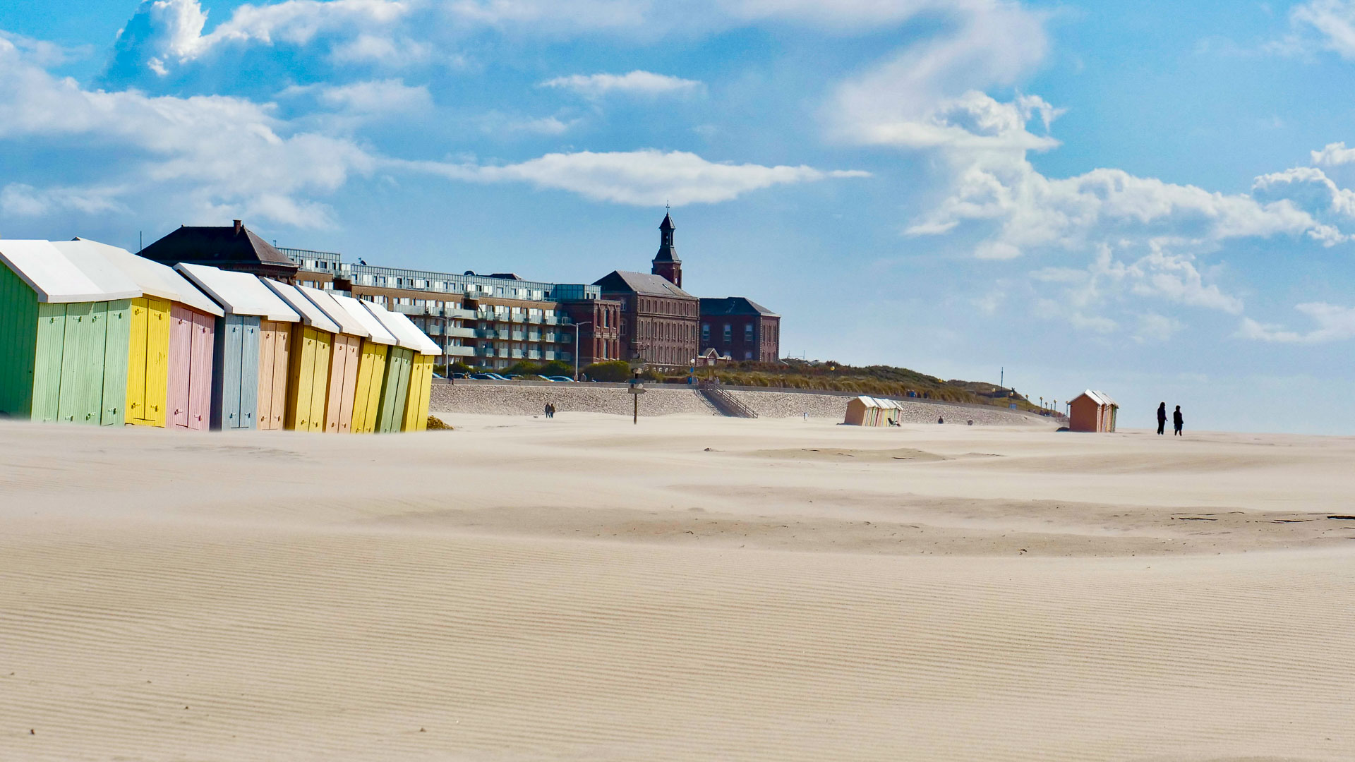 View of a long stretch of beach with coloured beach huts on the Opal Coast