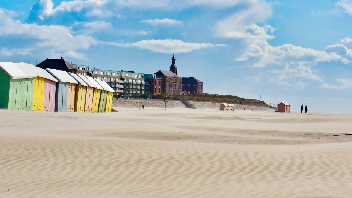View of a long stretch of beach with coloured beach huts on the Opal Coast