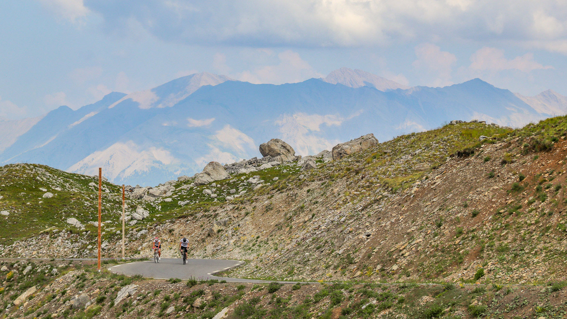 two road cyclists climbing the iconic col de la Bonette, the surrounding landscape is wide open and mineral